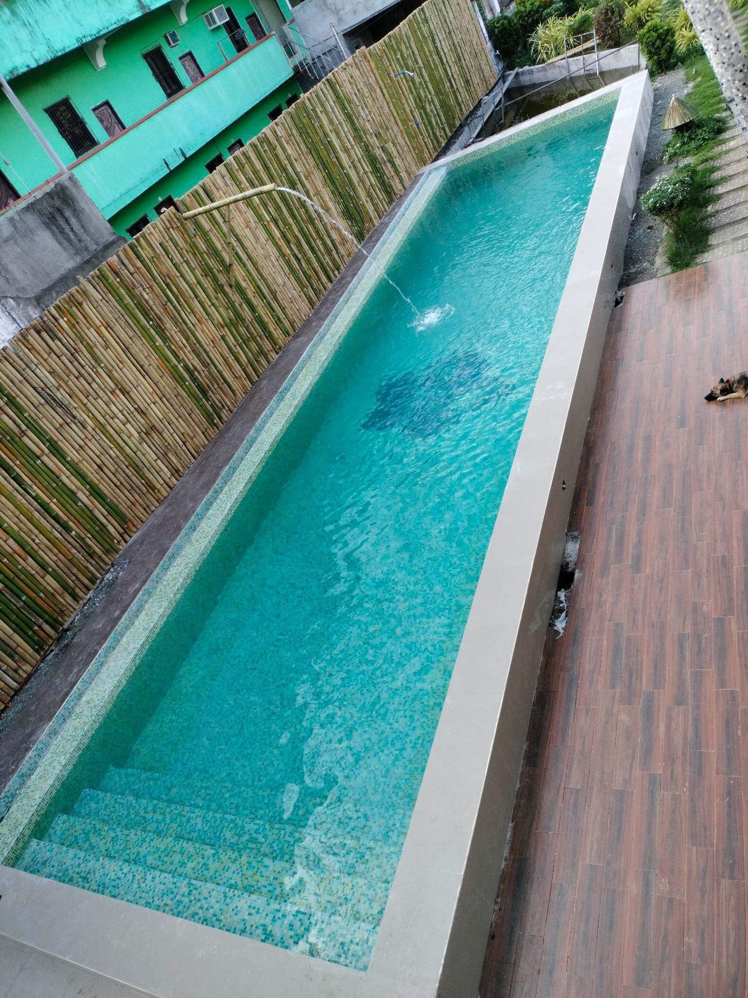 A rectangular swimming pool with clear blue water, surrounded by a bamboo fence and a tiled deck.