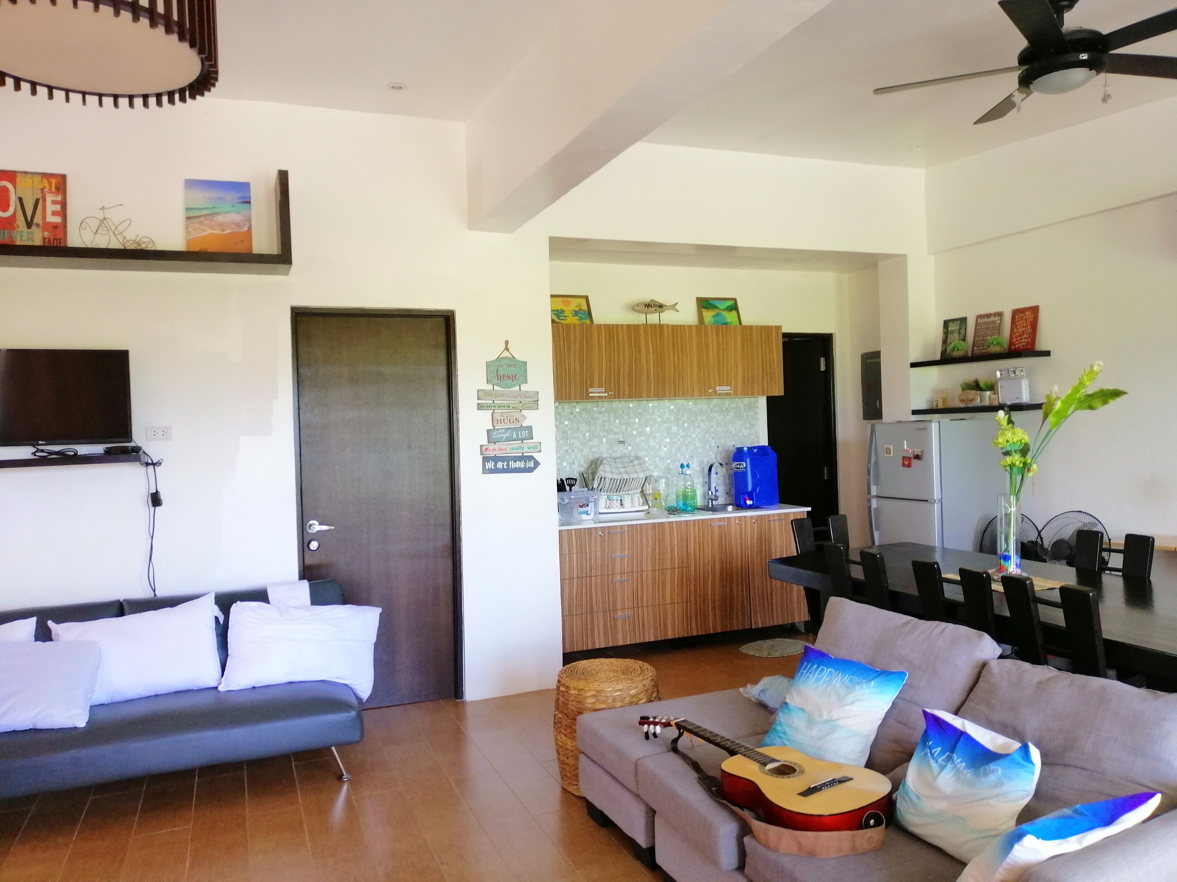 Una sala moderna con un sofá, una mesa de centro y una guitarra. Hay una zona de cocina con armarios de madera y un refrigerador.