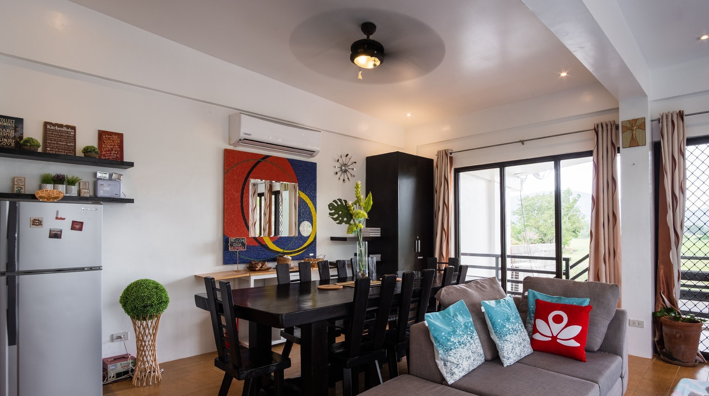 A modern kitchen with a dining area, a large window, and a ceiling fan.
