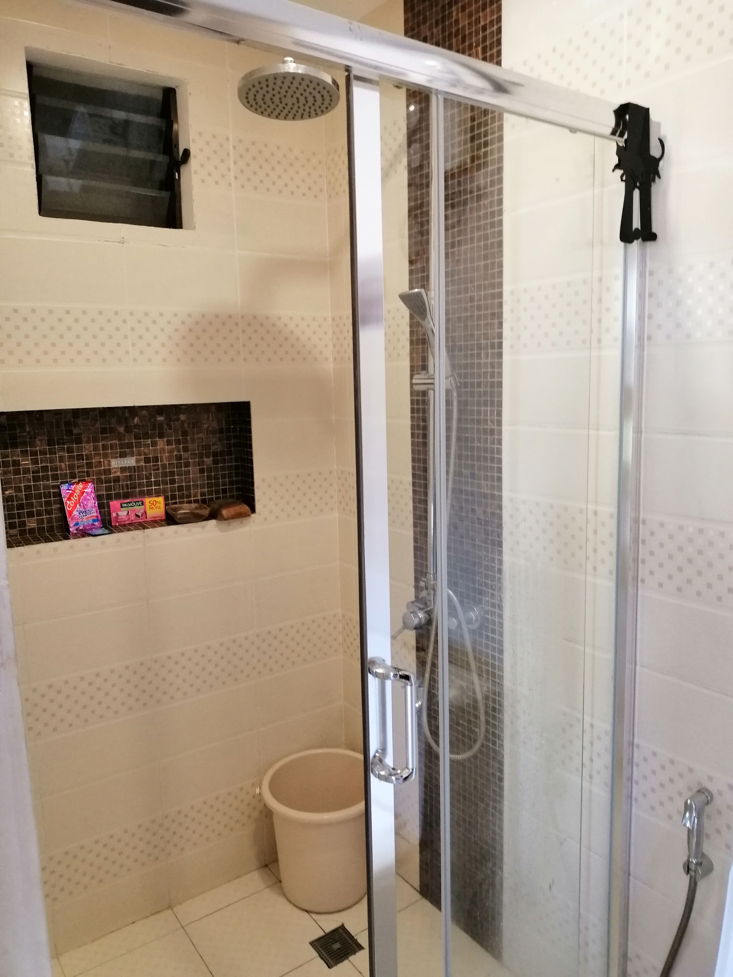 Un área de ducha con mampara de vidrio, un cabezal de ducha de mano y un grifo empotrado en la pared.