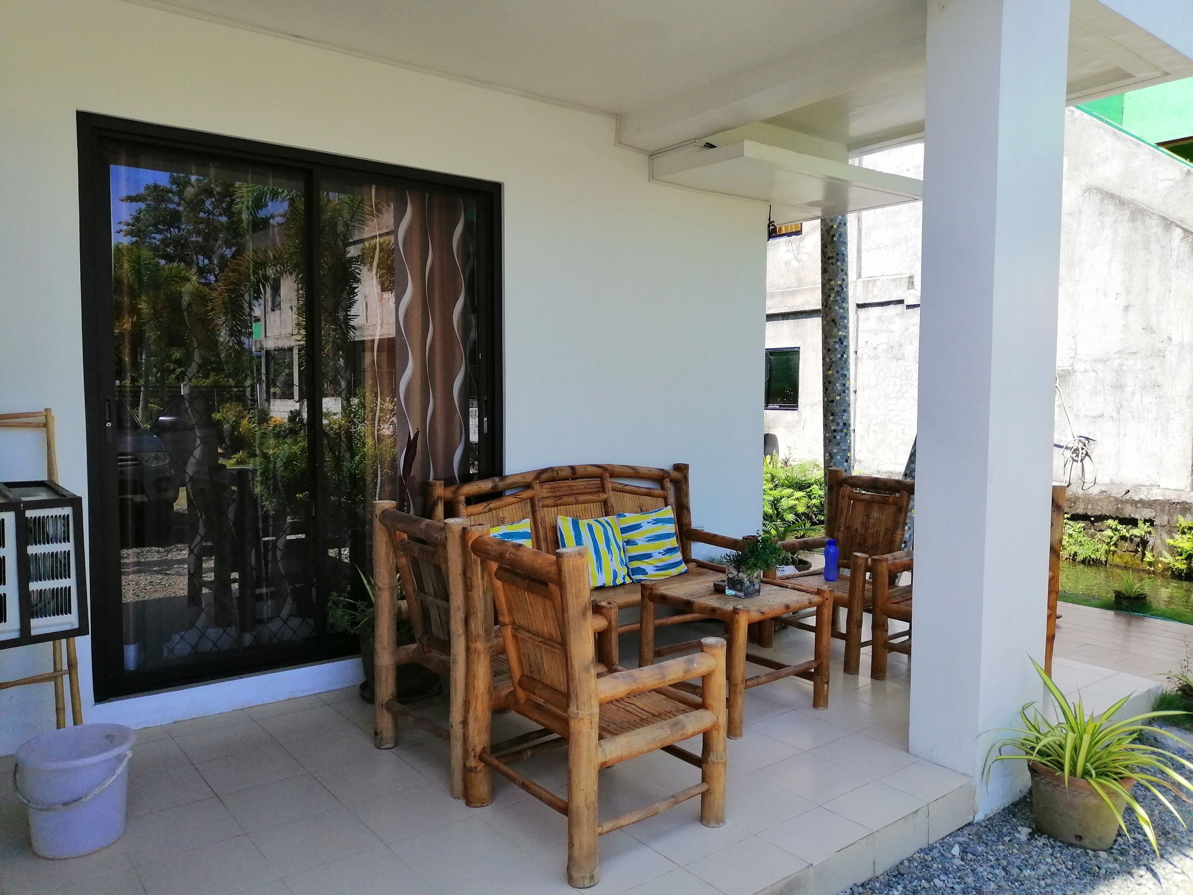 A covered outdoor seating area with wooden furniture and a glass door leading to a garden.