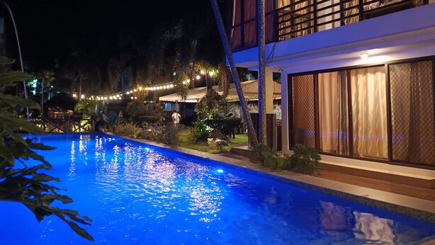A nighttime view of a hotel with a swimming pool, a covered outdoor area, and a two-story building with large windows and a balcony. - Casa Herminia Baler (Baler)