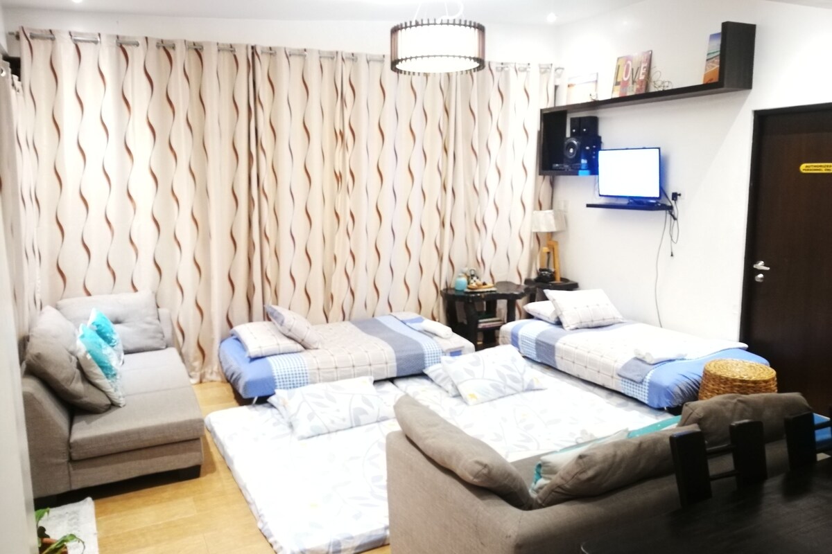A room with two beds, a sofa, a TV, and a door.