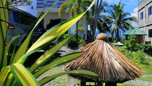 A modern building with a flat roof, surrounded by tropical vegetation and a thatched structure. - Casa Herminia Baler (Baler)