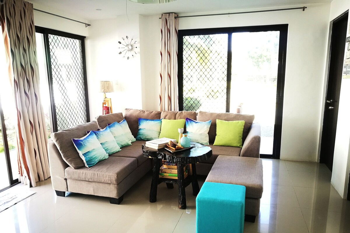 A living room with a sectional sofa, a coffee table, and a teal ottoman.