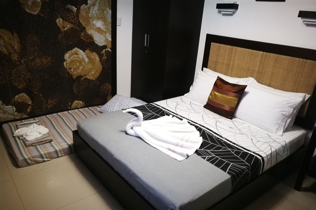 A hotel room with a bed, a nightstand, a wall-mounted lamp, and a painting.