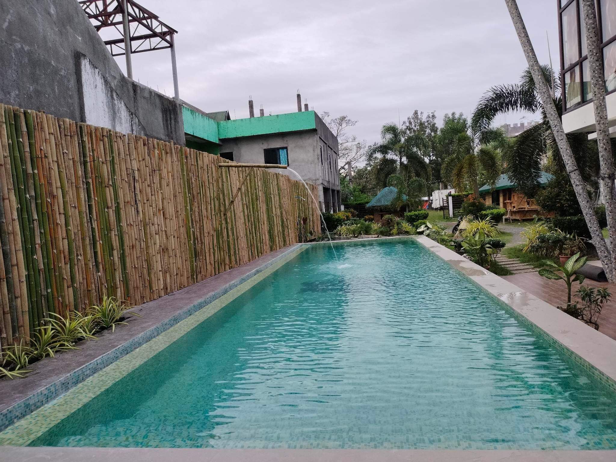 Una piscina rectangular con agua cristalina, rodeada por una cerca de bambú y un muro de hormigón.