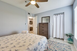 A bedroom with a bed, a dresser, a mirror, a ceiling fan, and a window with a curtain. - Pool Access, Walk to Manatee Beach: Coastal Condo (Holmes Beach)