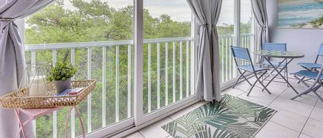 A balcony with a view of trees, a ceiling fan, and a table with chairs.