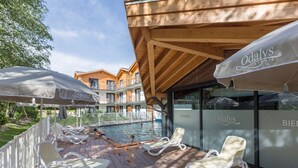 A poolside area with lounge chairs and umbrellas, a wooden deck, and a building with balconies.