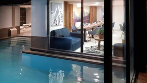 A pool area with a blue pool, a seating area with a blue sofa and chairs, and a dining area with tables and chairs.