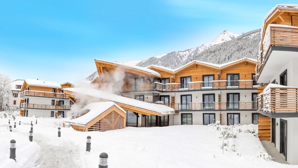 A snow-covered resort with wooden buildings, a ski lift, and a mountain backdrop.