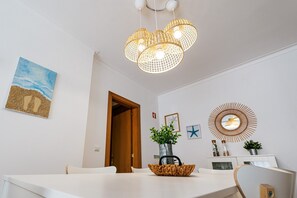 A dining area with a white table, a wicker basket, a potted plant, and a wall-mounted decorative mirror.