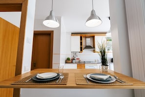 A dining area with two tables set for two, each with plates, cutlery, and napkins. There are two pendant lights above the tables.