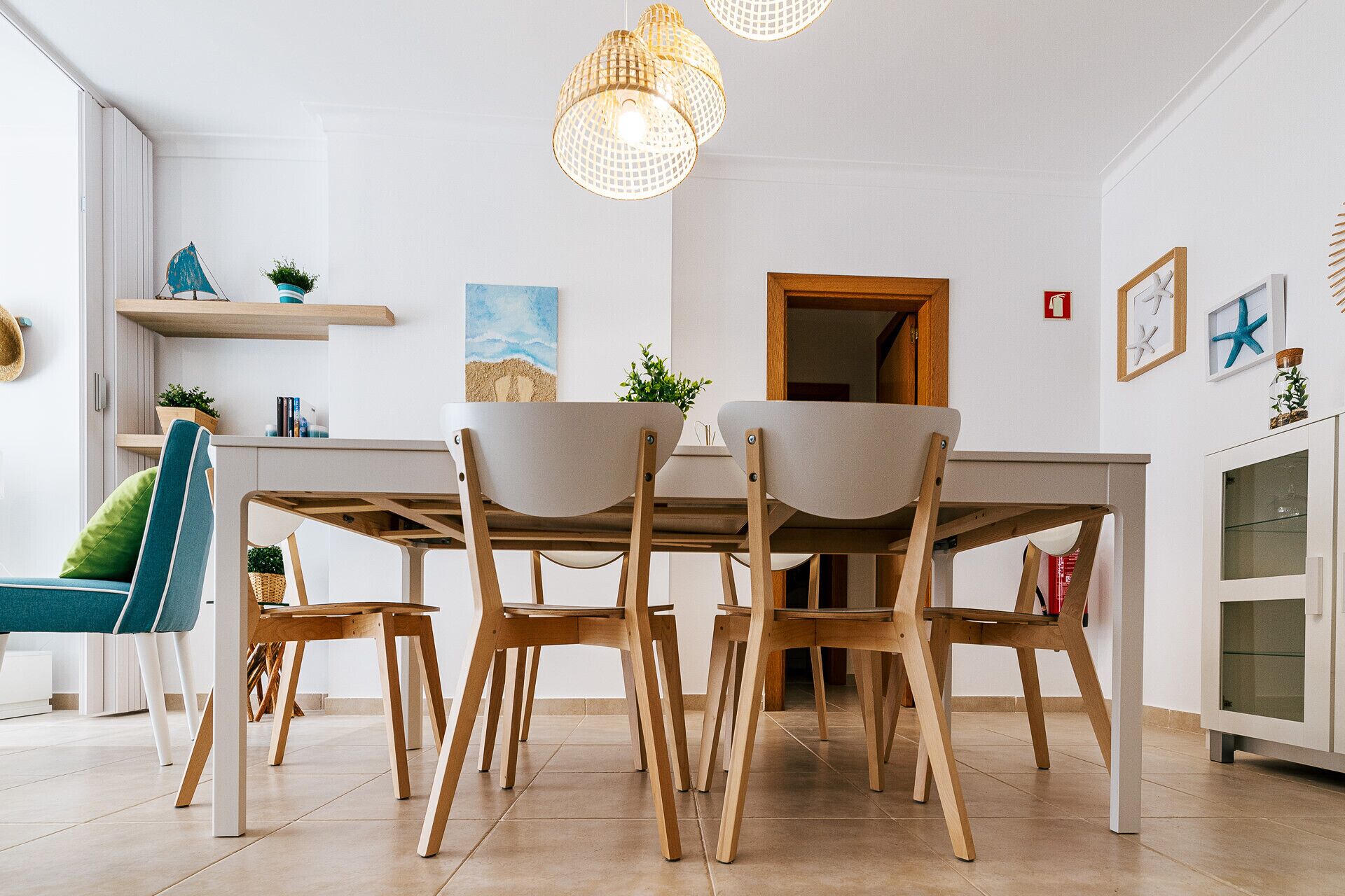 A modern dining area with a wooden table and chairs, pendant lighting, and a view of the kitchen.