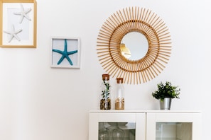 A white wall with a circular wooden wall art, two framed starfish, a small cabinet with glass doors, and a potted plant.