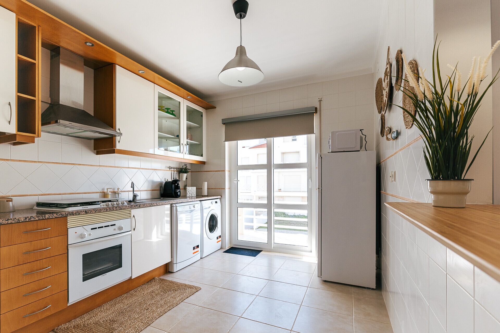 A modern kitchen with wooden cabinets, a built-in oven, a microwave, and a washing machine.