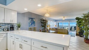 Une cuisine moderne avec des meubles blancs, un grand îlot central et un coin repas agrémenté d’un canapé jaune.