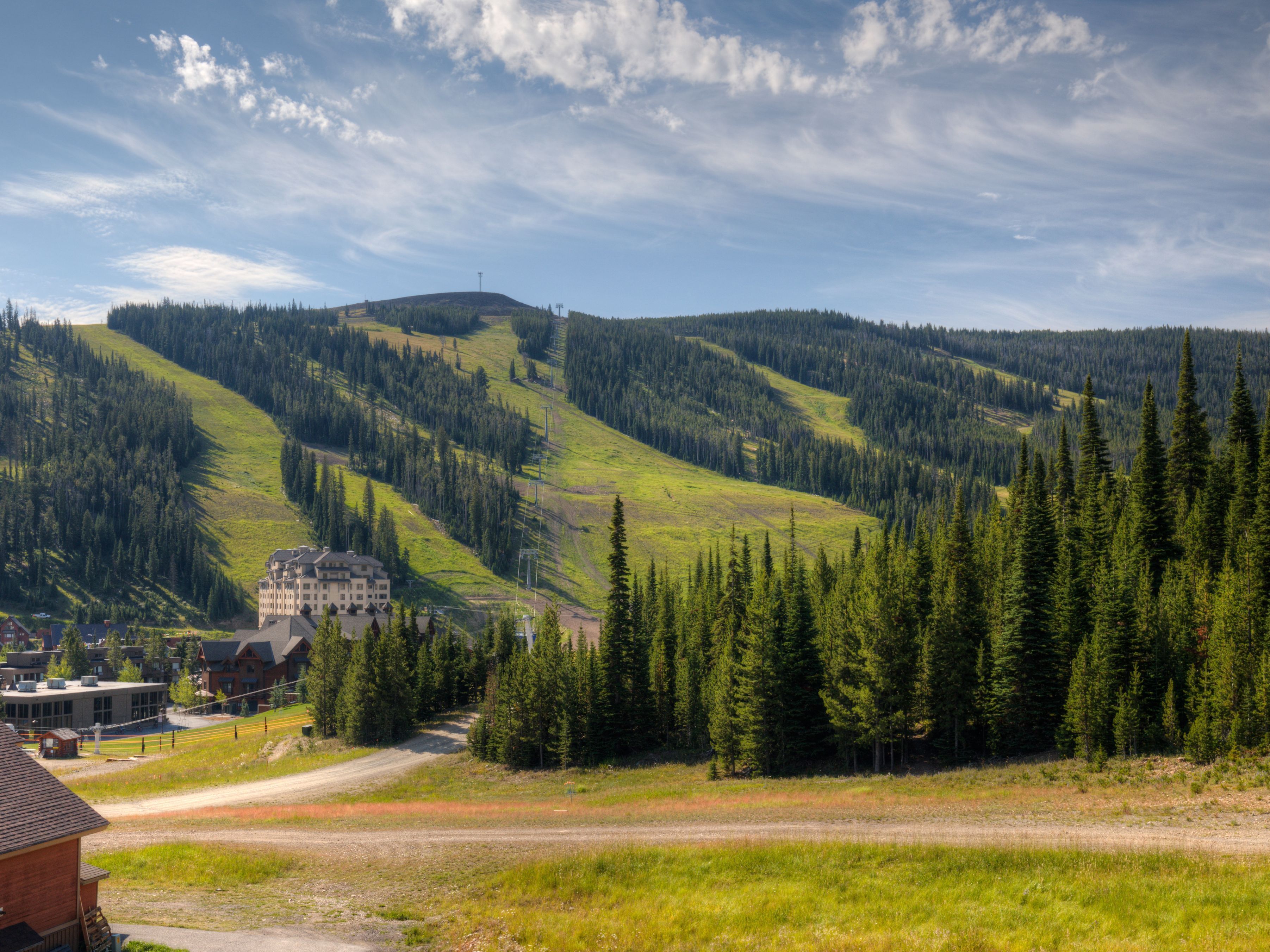 A mountain lodge with a large building and a smaller structure, surrounded by dense forest and rolling hills.