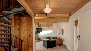 Interior de madera con suelo de piedra, una escalera, una chimenea de piedra y vistas al exterior.