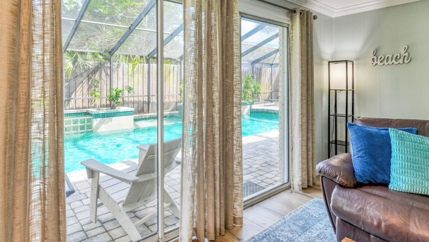 Habitació amb vista a una piscina exterior, un sofà de pell amb coixins i una làmpada de peu.