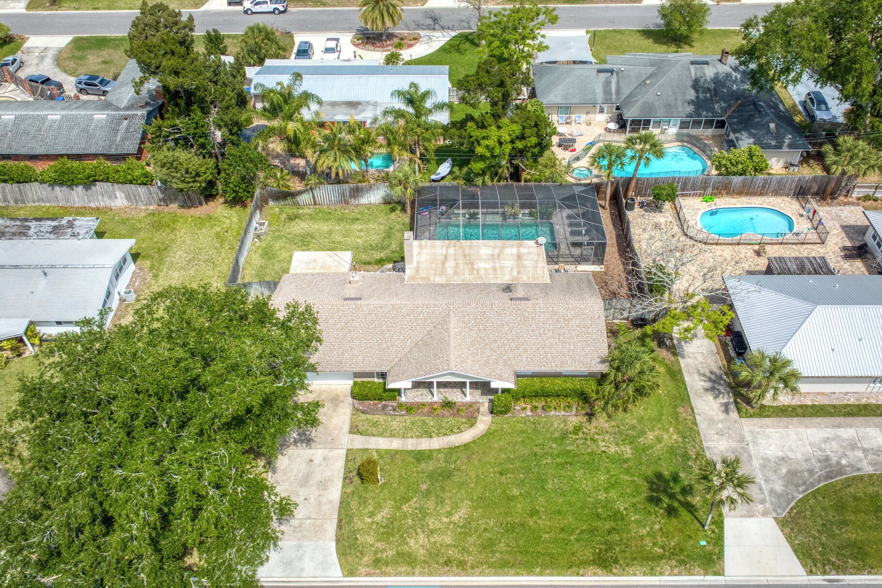 Un barrio residencial con una casa que tiene un amplio patio trasero, una piscina y un porche cubierto.