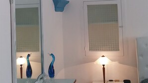 Un dormitorio con techo blanco, un espejo con marco decorativo, una mesita de noche con lámpara y una cama con cabecera azul.