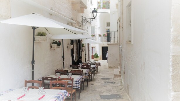 Un café al aire libre con mesas y sillas, sombrillas blancas y plantas en macetas.