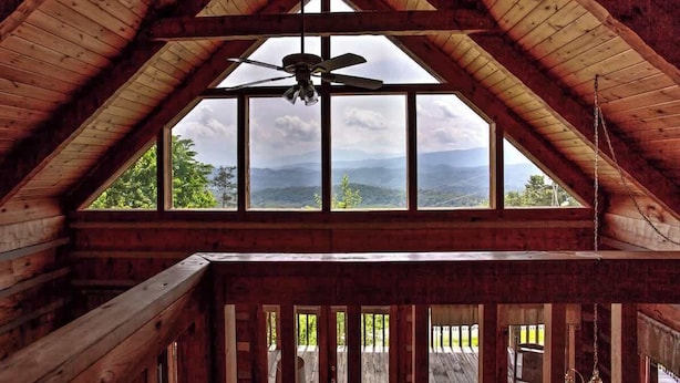 A wooden cabin with a sloped roof, a ceiling fan, and large windows offering a view of the mountains. - Super View,Smoky Mtn Log Cabin,Pool Table,Hot Tub (Sevierville)