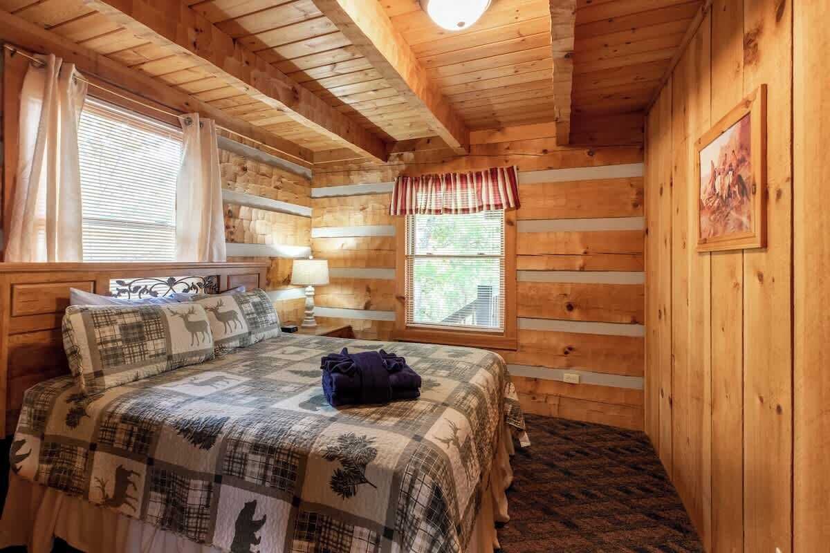 Une chambre dans une cabane en bois, avec un lit, des rideaux, une fenêtre et une lampe.