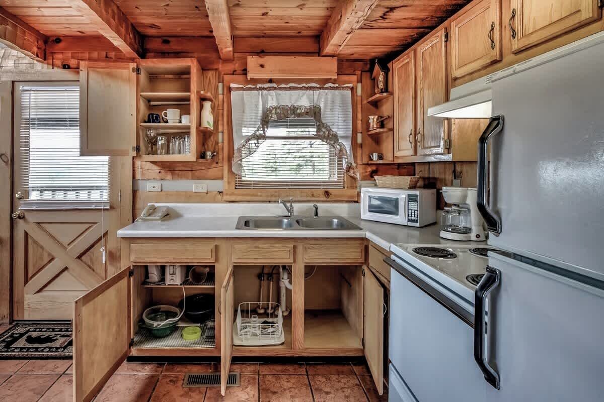 Une cuisine compacte dotée de meubles en bois, d’un plan de travail blanc, d’un évier, d’un four à micro-ondes et d’un réfrigérateur.