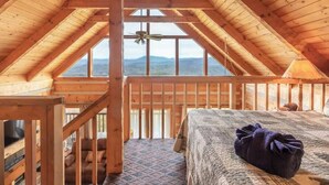 A wooden cabin with a high ceiling, a bed with a blanket, a television, and a view of mountains through large windows. - Super View,Smoky Mtn Log Cabin,Pool Table,Hot Tub (Sevierville)