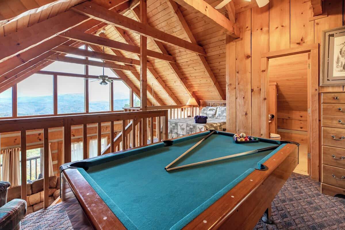 A pool table in a wooden room with a high ceiling and a view of the mountains.