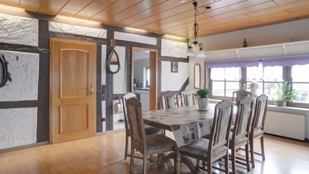 Zona pranzo con tavolo e sedie in legno, pareti in pietra e soffitto con travi a vista.