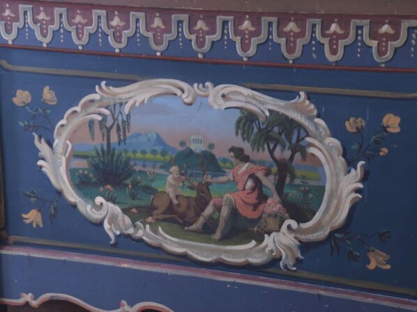 Une fresque murale avec un cadre ovale central représentant une scène pastorale avec des personnes et des animaux.