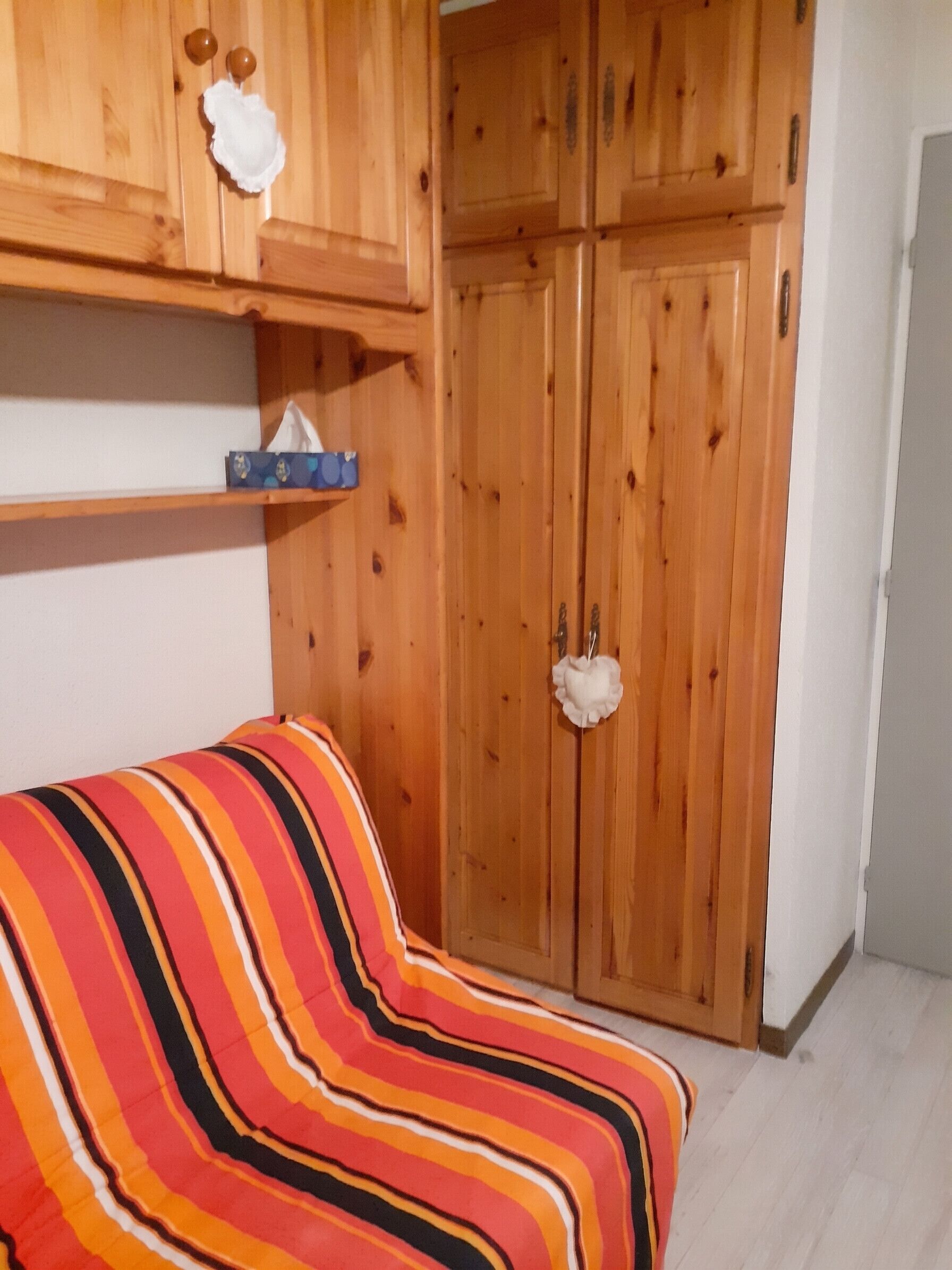 Una habitación con sofá a rayas, un armario de madera y una estantería con objetos.