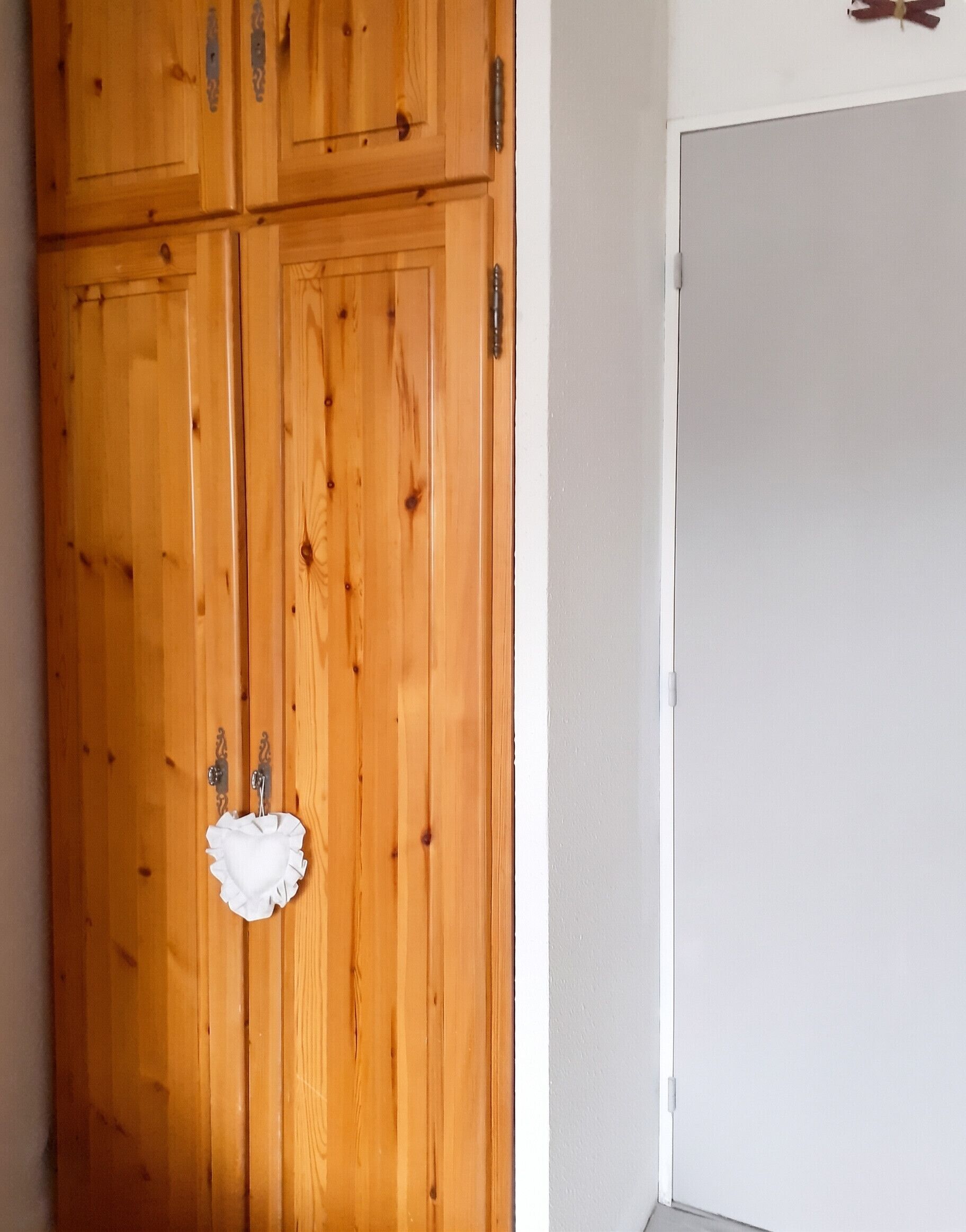 Une armoire en bois avec une porte blanche, un petit objet blanc accroché à la porte et un mur blanc adjacent.