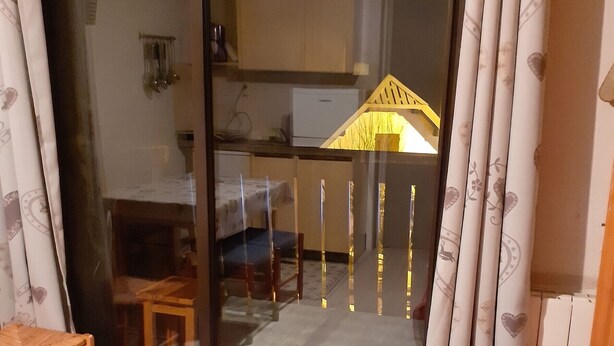 A room with a sliding glass door leading to a balcony, a small wooden stool, a colorful striped blanket, and a patterned curtain. - Homerez - Studio in Allos - mountain view (Allos)