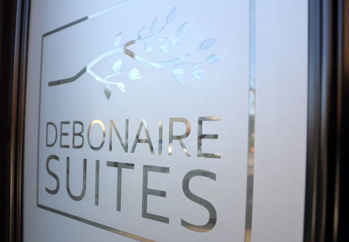 Une enseigne portant l'inscription « DEBONAIRE SUITES » et ornée d'un motif décoratif en forme de branche.