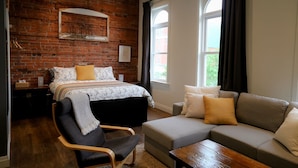 A modern bedroom with a brick wall, a bed with a striped blanket, a grey sofa, and a wooden coffee table.