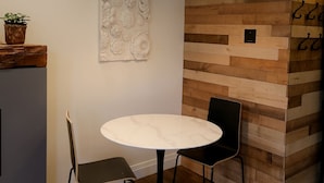 A modern dining area with a round table, two chairs, a pendant light, and a decorative wall panel.
