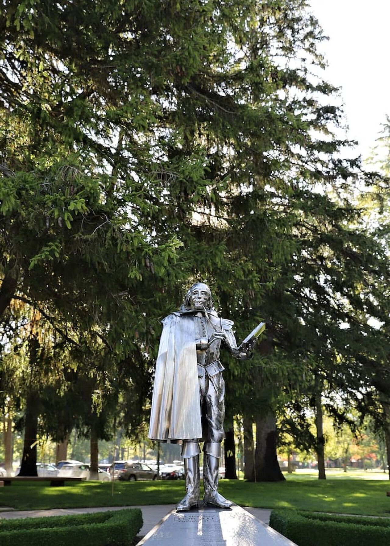 A statue of a historical figure in a park with trees and a paved path.