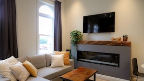 A modern living room with a sofa, a coffee table, a fireplace, and a flat-screen TV mounted above it.
