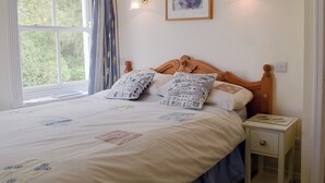 Ein ordentlich bezogenes Bett mit gemusterten Kissen, ein Nachttisch mit Schublade und ein gerahmtes Kunstwerk darüber.