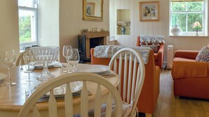 Ein Essbereich mit Tisch für vier Personen, Kamin und einer Couch in einem Raum mit Holzbalken und großen Fenstern.