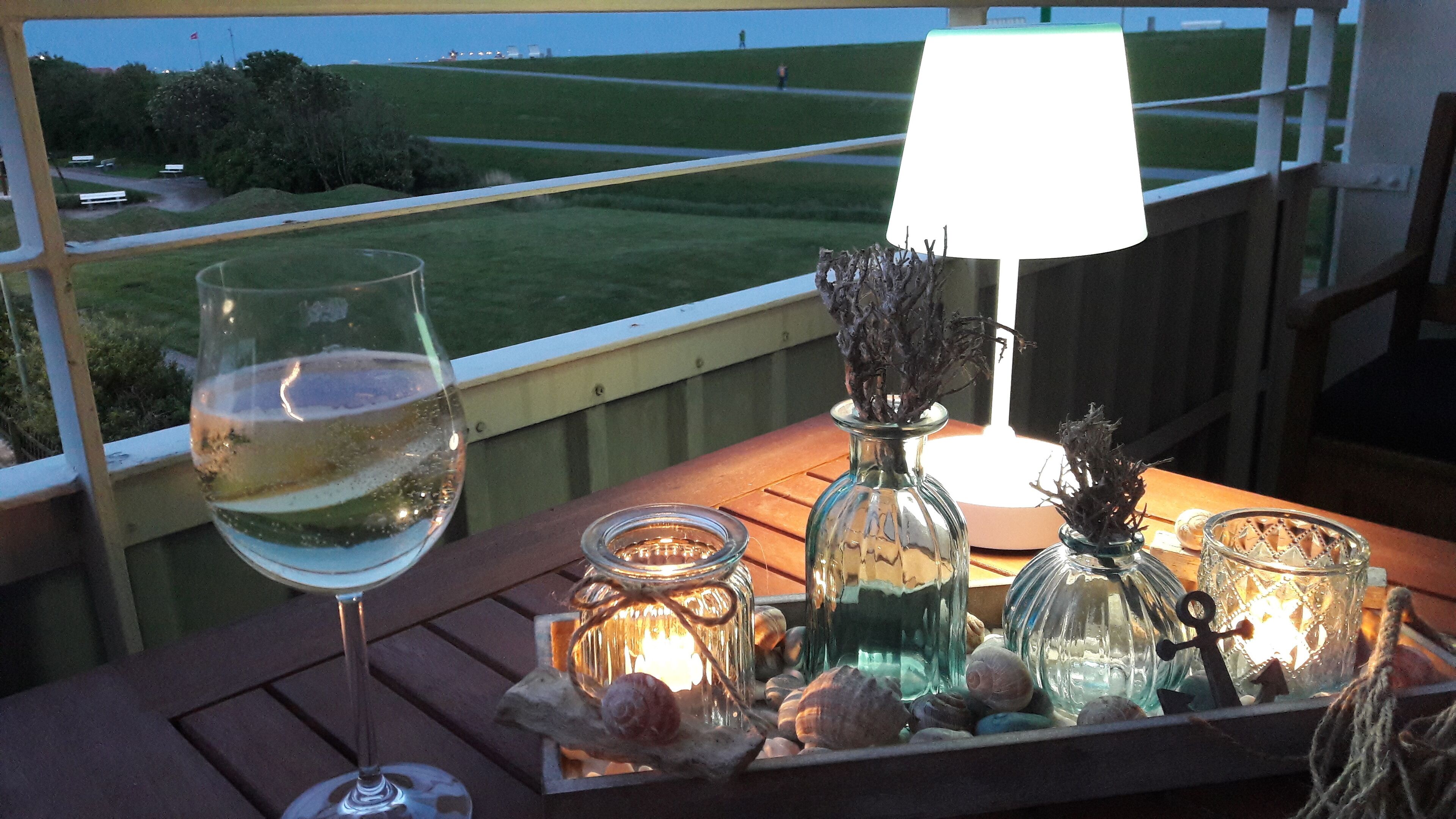 A table with a glass of white wine, a lamp, and decorative jars with seashells and candles.