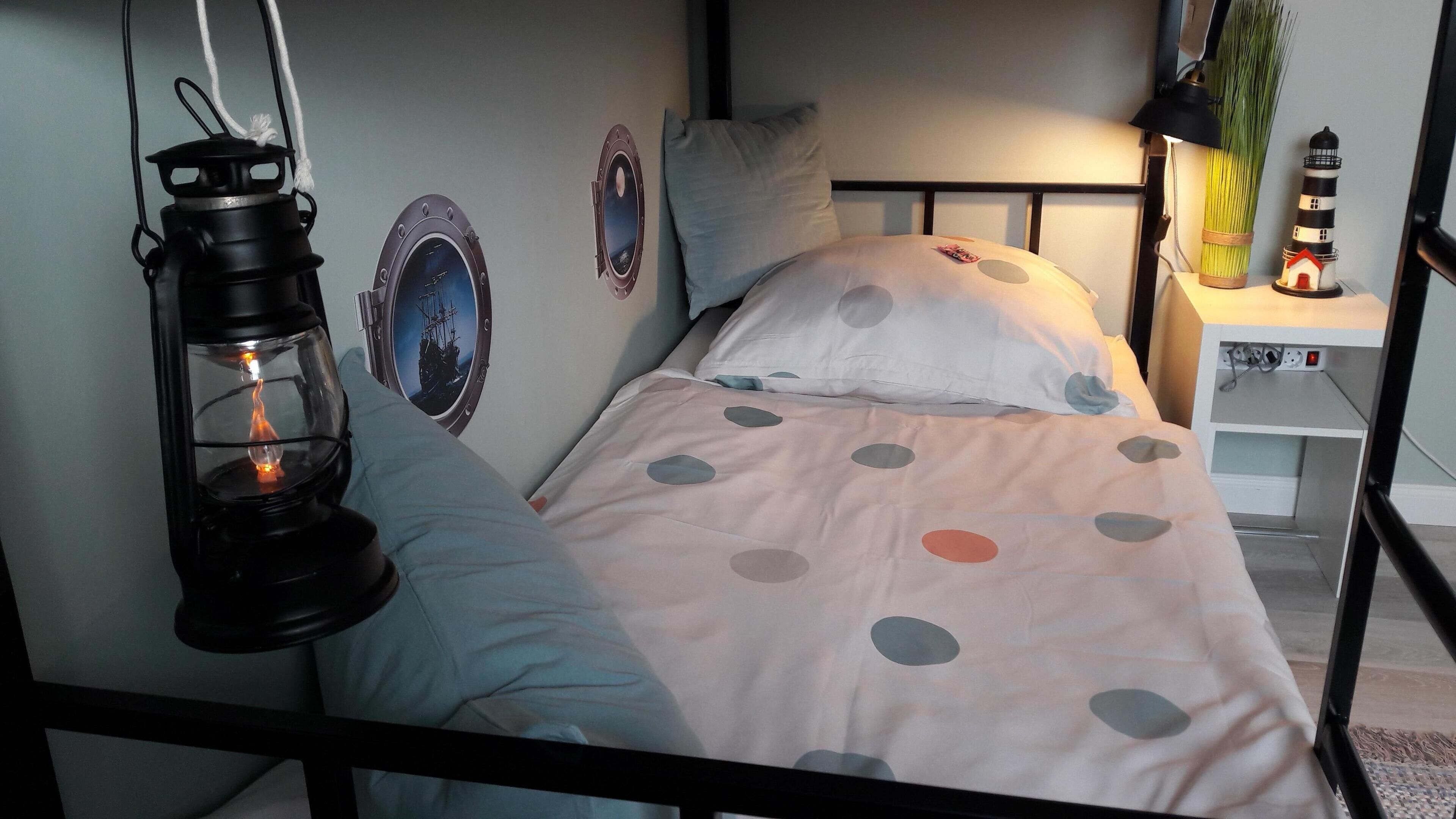 A bed with a polka dot bedspread, a hanging lantern, and a wall-mounted window with a ship image.