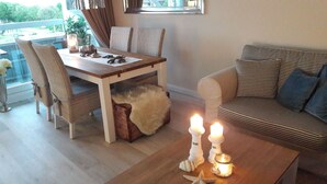 A dining area with a wooden table, wicker chairs, a fluffy rug, and a striped sofa. Candles are placed on the table and a small jar with a starfish decoration. - Sea view, balcony, 3 room apartment (Büsum)