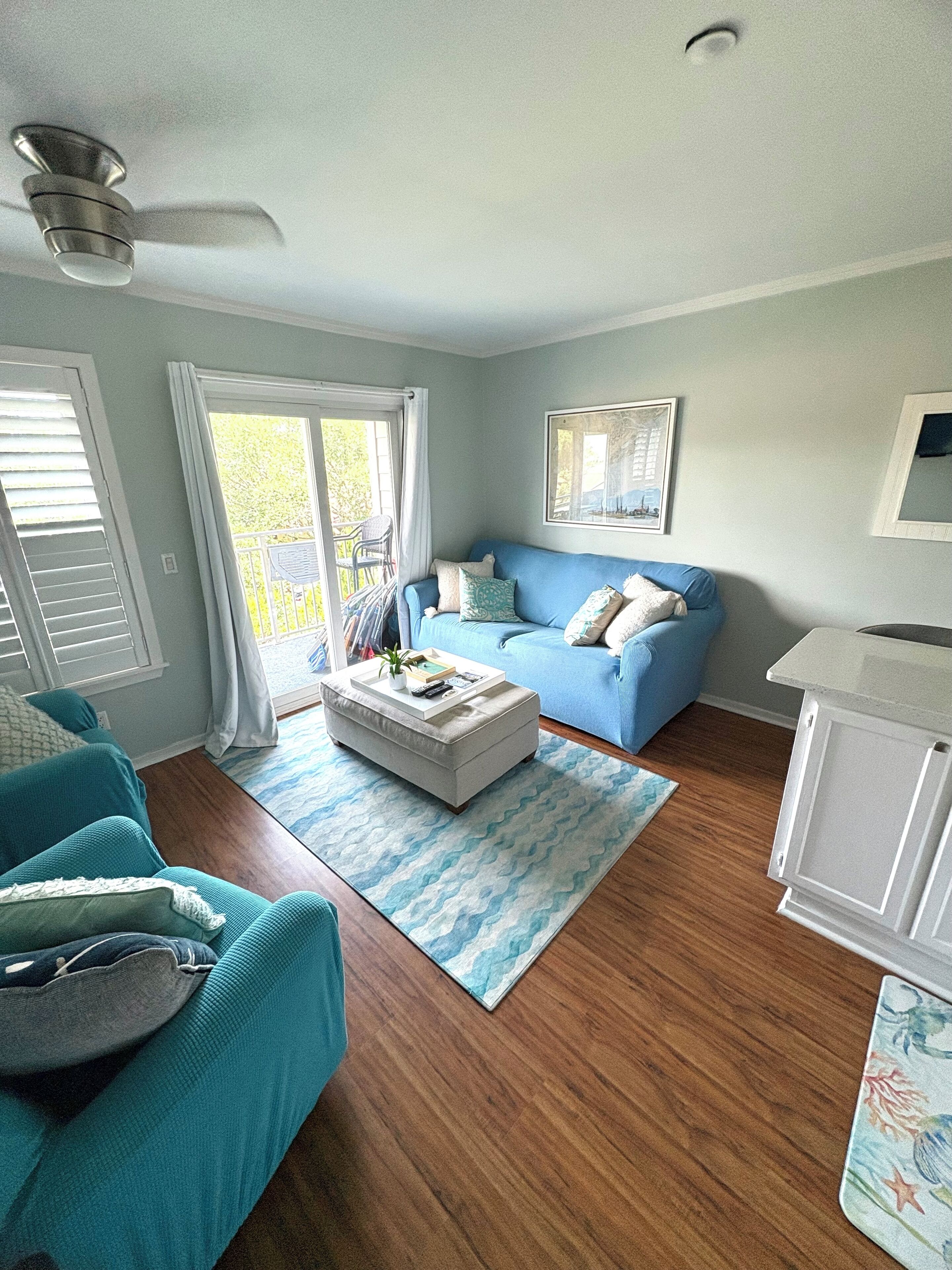A living room with a blue sofa, a white ottoman, and a ceiling fan.