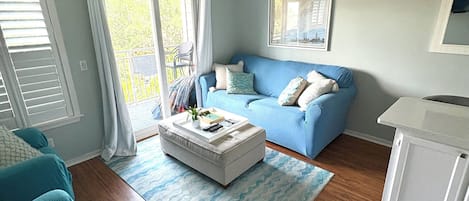 A living room with a blue sofa, a white ottoman, and a ceiling fan.